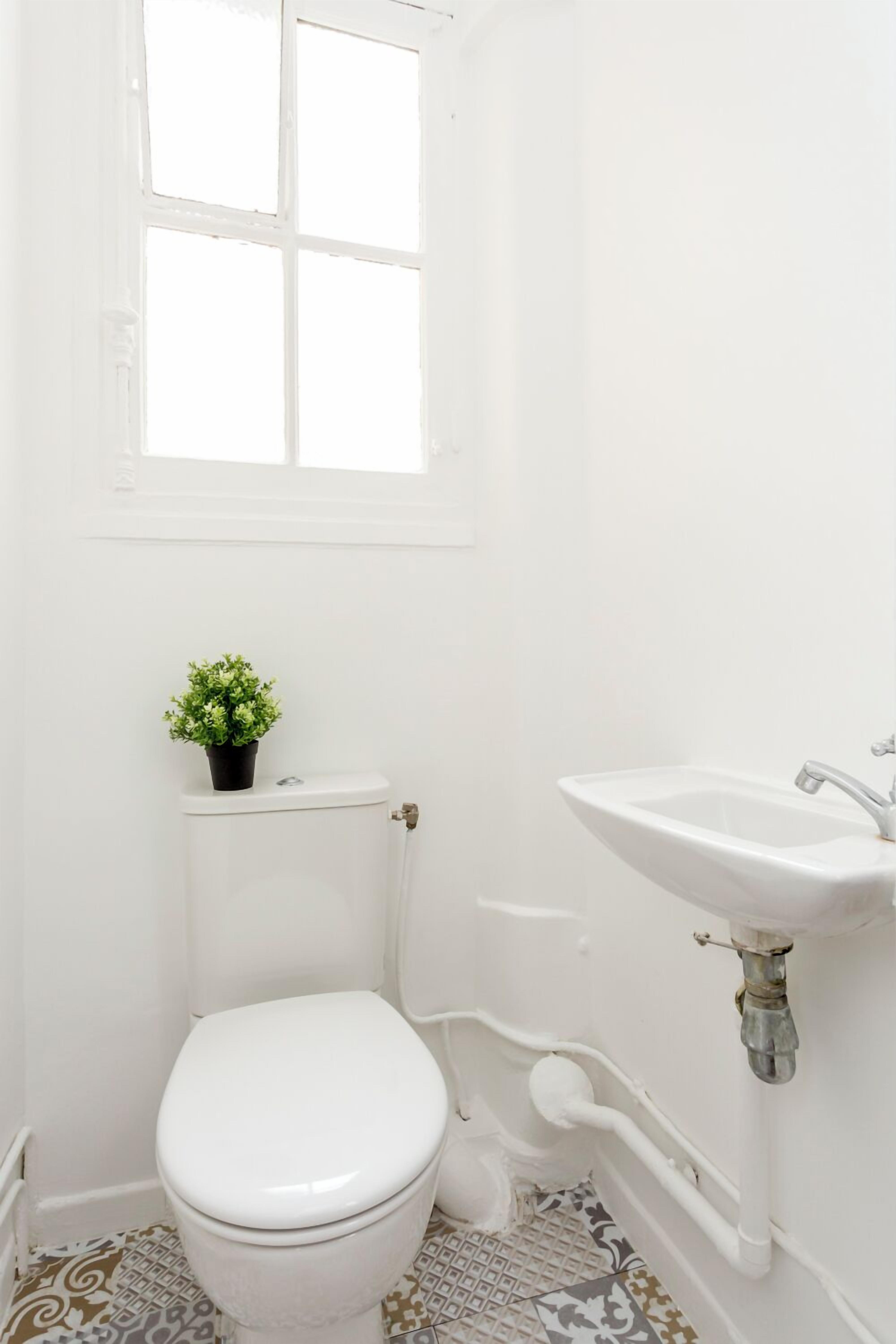 A small, white bathroom with a toilet, a sink, and a window.