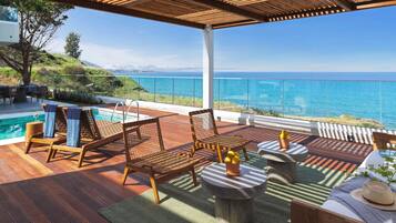 Una terraza de madera con mobiliario exterior, piscina y vista al mar.
