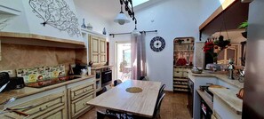 A kitchen with a dining area, a clock, and a decorative wall piece. - Villa Elisa, Cllim, Wifi,Swimming pool, 5 Km from beaches. (Figari)
