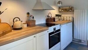 Una cuina moderna amb armaris blancs, tauleig de fusta, un búllet, una cafetera i forn de pared.