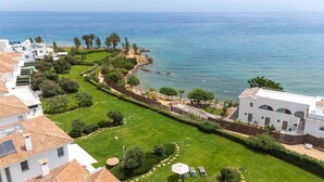 Une propriété située sur la côte, dotée d’une pelouse bien entretenue, d’un sentier menant à la mer et d’un bâtiment blanc orné d’arcades.
