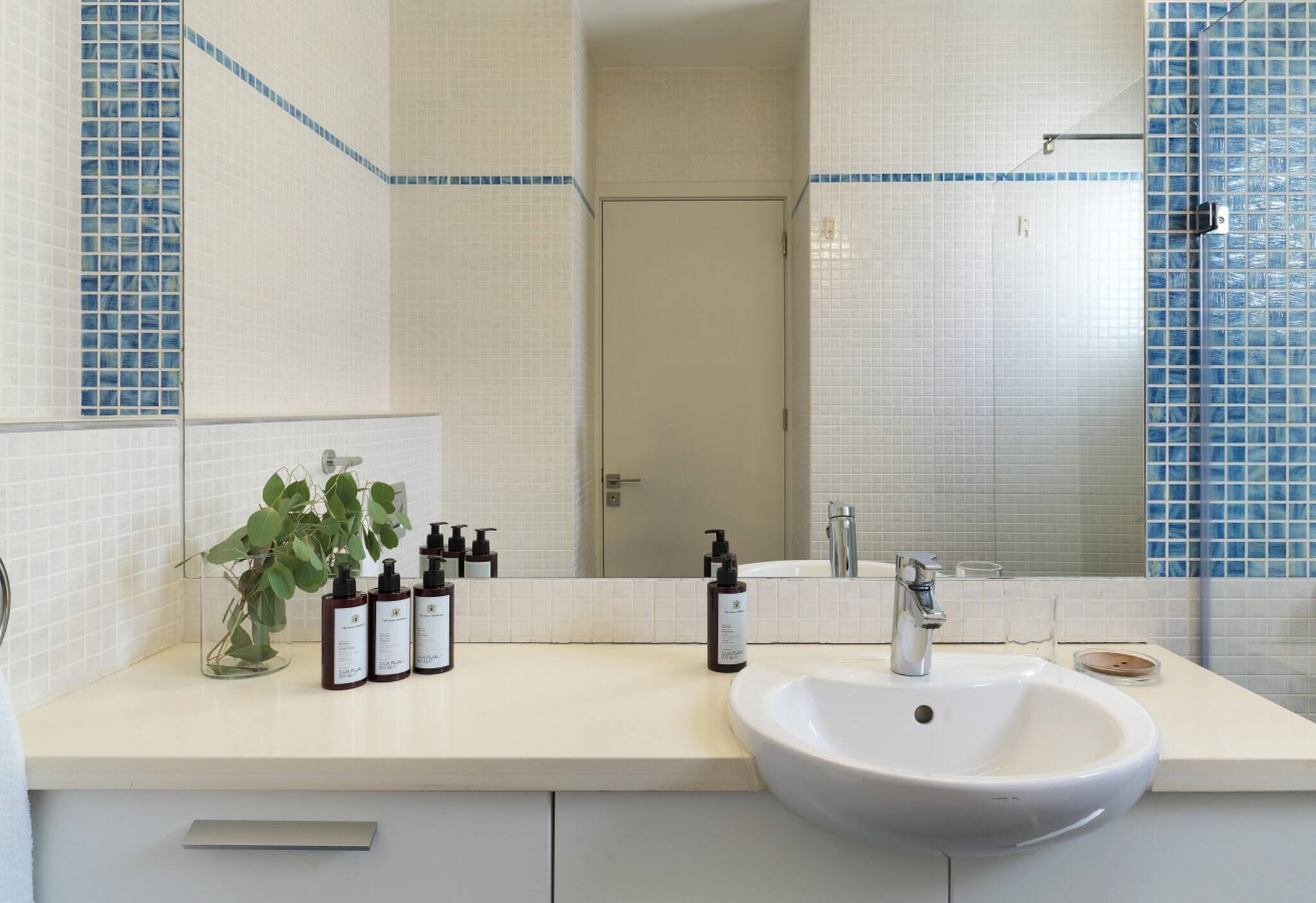 A bathroom with a white sink, a mirror, and toiletries on the counter.