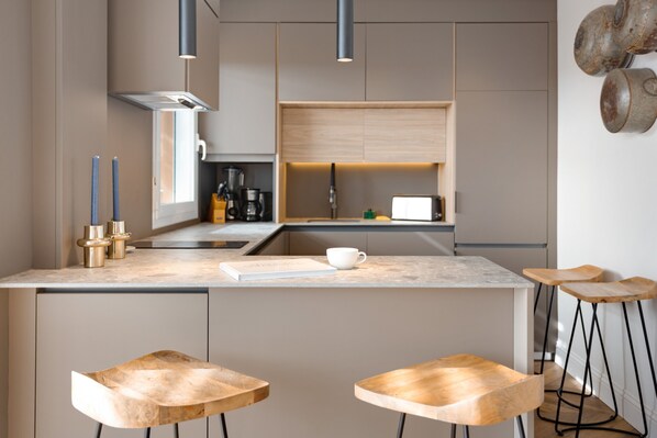 A modern kitchen with a central island, bar stools, pendant lighting, and a coffee machine.