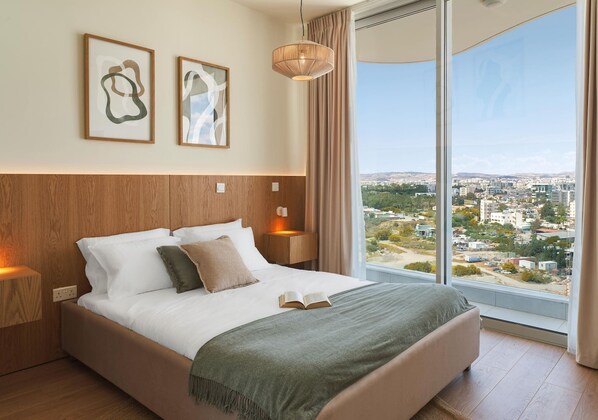 Habitación de hotel moderna con una cama grande, dos lámparas de noche, vistas de la ciudad y arte abstracto en la pared.