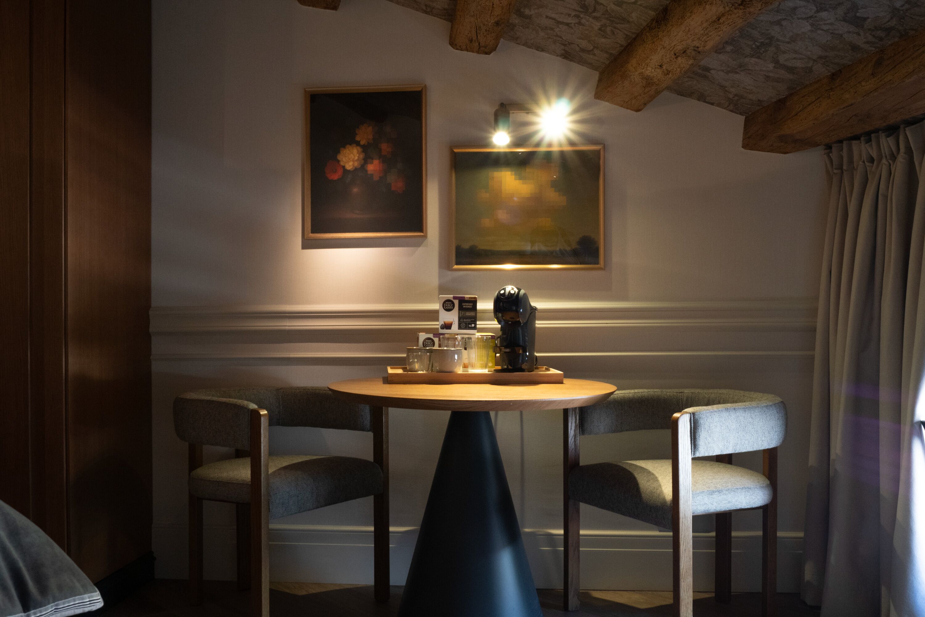 A cozy dining area with a round table, two chairs, and two framed artworks on the wall.