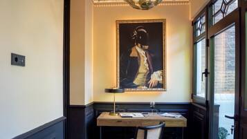 Una habitación con escritorio, un retrato en la pared y una ventana.