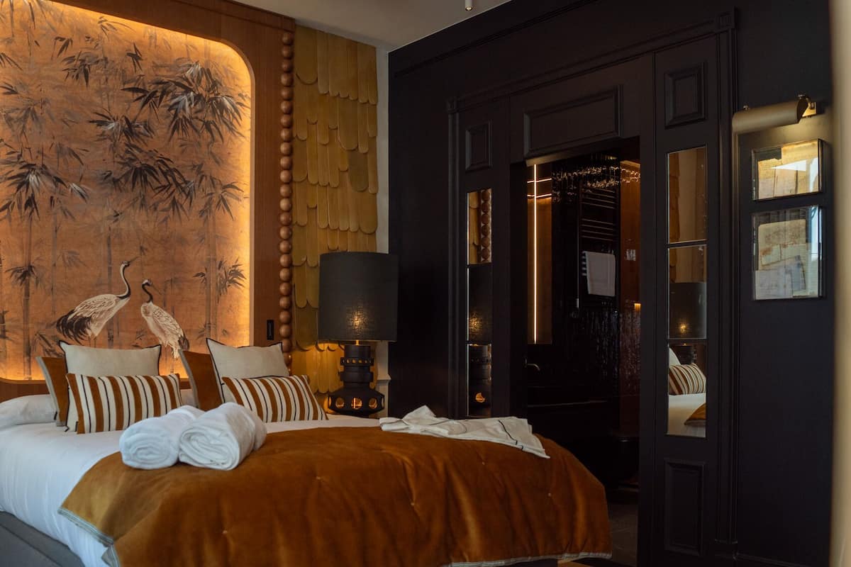 Habitación de hotel con cama, almohadas, lámpara y una pared con diseño de bambú.