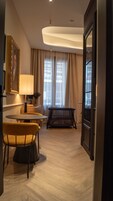Habitación de hotel con zona de comedor, sofá, lámpara, ventana con cortinas y una puerta.