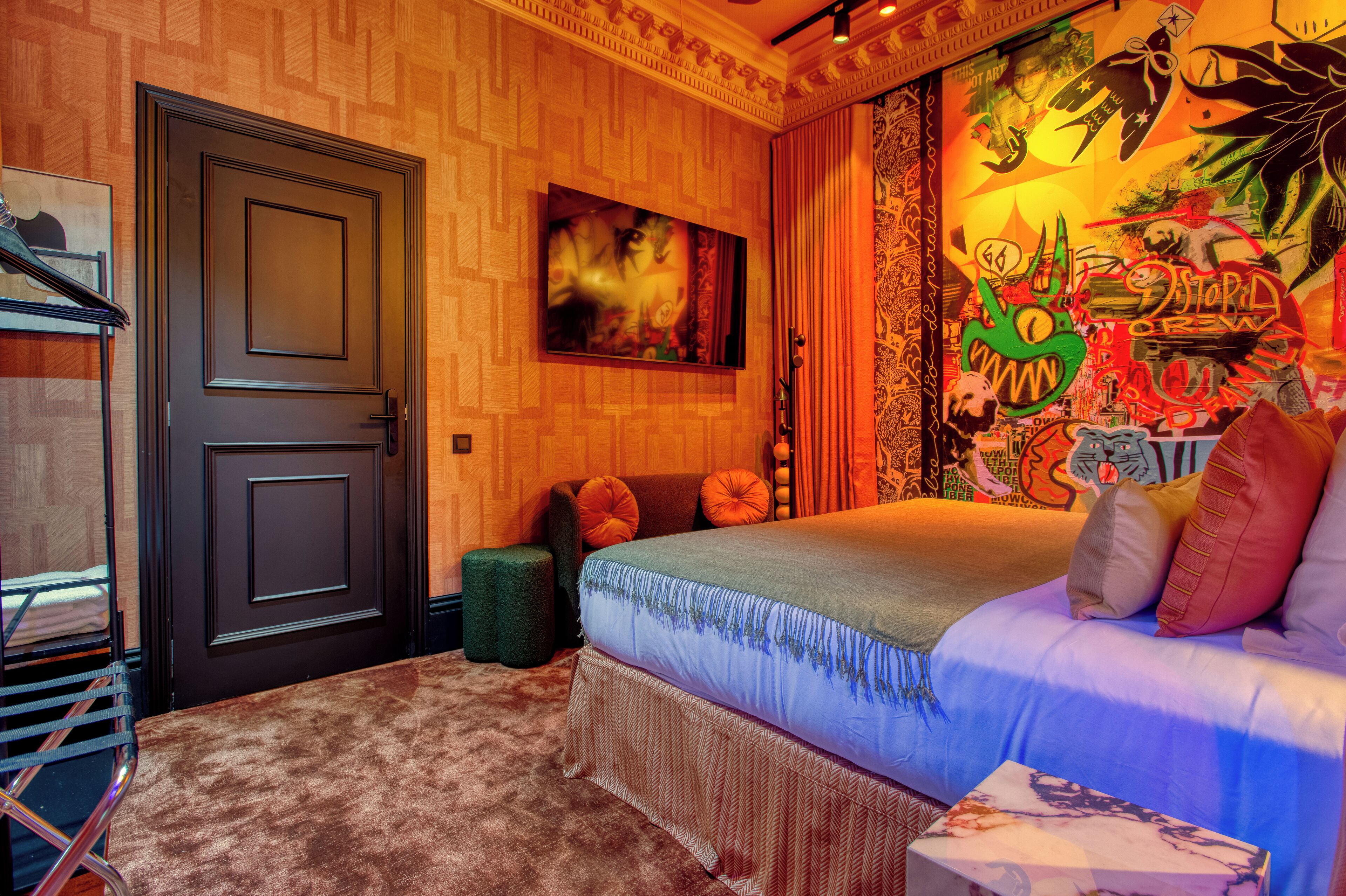 A bedroom with a bed, a door, a wall-mounted artwork, and a patterned wall.