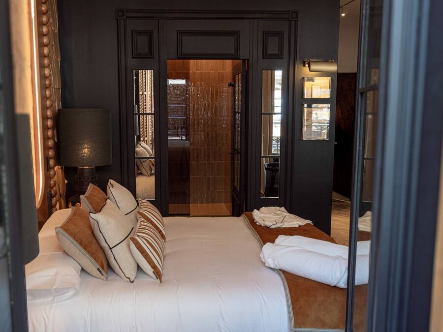 Ein Hotelzimmer mit einem großen Bett, einem Nachttisch, einer Lampe und Blick ins Freie.