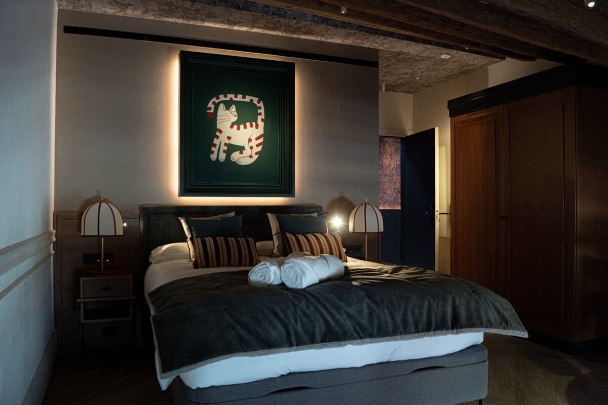 Un letto rifatto con un copriletto scuro e cuscini, un quadro incorniciato sopra e un armadio in legno sulla destra.