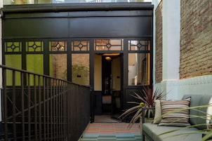 Una entrada moderna con un portón negro, una escalera y un área de descanso con cojines estampados.