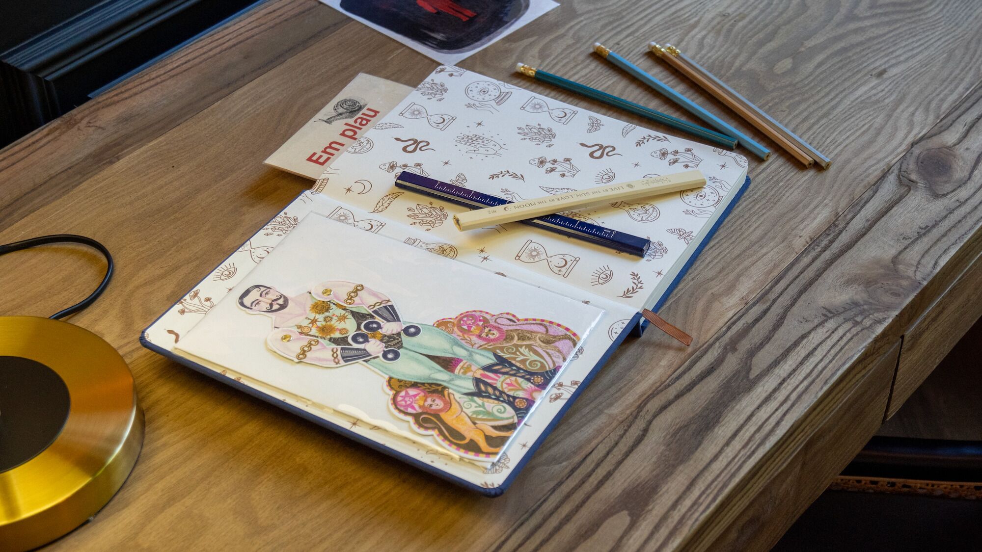 Ein Notizbuch mit farbenfroher Illustration auf dem Einband, platziert auf einem Holztisch.