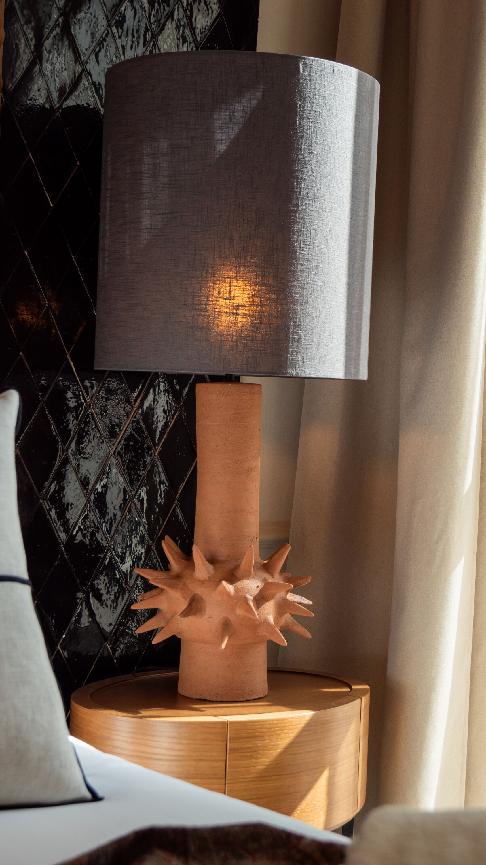 A modern lamp with a textured shade and a unique, spiky base on a wooden nightstand.
