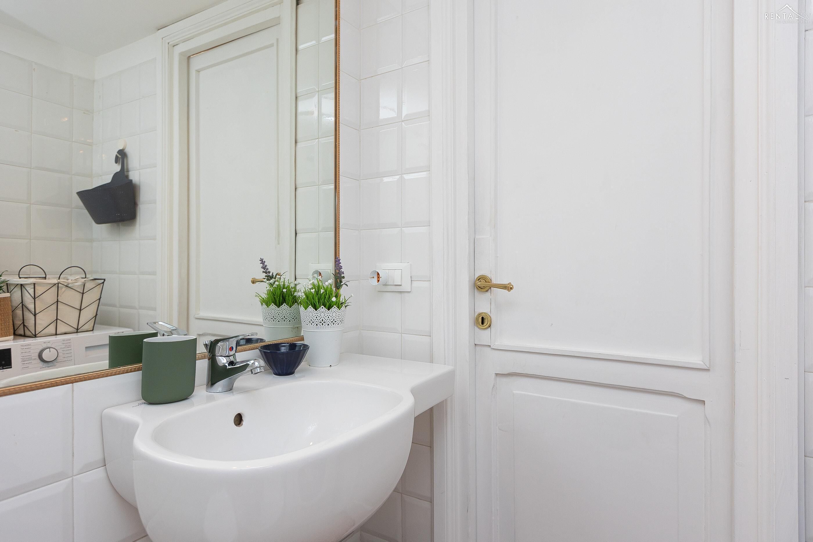 A bathroom with a white sink, a mirror, and a door with a golden handle.