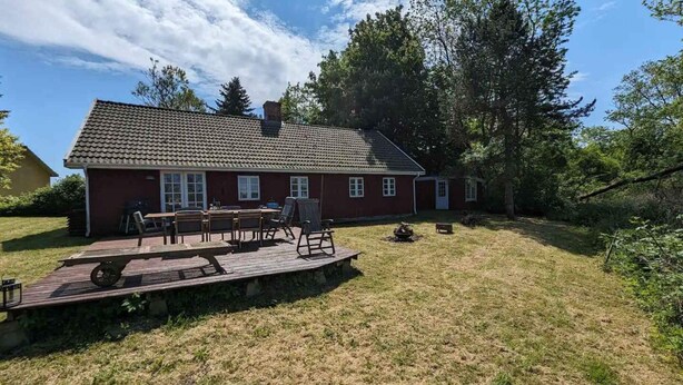 A red house with a tiled roof, a deck with outdoor furniture, and a grassy yard.