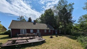 A red house with a tiled roof, a deck with outdoor furniture, and a grassy yard.