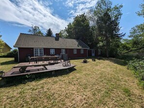 A red house with a tiled roof, a deck with outdoor furniture, and a grassy yard.