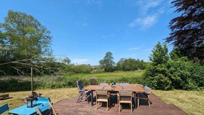 An outdoor wooden deck with a large table and chairs, surrounded by greenery and trees. - 5 Star Holiday Home in Vesterborg (Vesterborg)