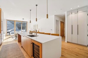 Una cocina moderna con una isla central, luces colgantes y vistas a un paisaje nevado a través de grandes ventanales.