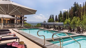 Un espace piscine aménagé sur le toit, avec des chaises longues, des parasols et une vue sur les montagnes.