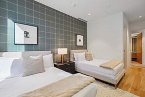 A hotel room with two beds, a nightstand with a lamp, and a large window.