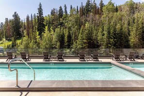 Ein Pool mit klarem, blauem Wasser, umgeben von Liegestühlen und einem bewaldeten Hang im Hintergrund.