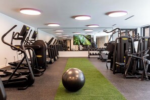 Ein Fitnessraum mit Laufbändern, Crosstrainern und einem großen Trainingsball auf Kunstrasen.