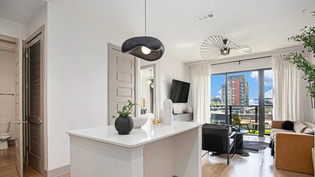 A modern apartment with a kitchen island, a living area with a sofa and chairs, a large window with a city view, and a balcony with a plant. - The first choice-vacation rental (Atlanta)