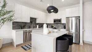 A modern kitchen with white cabinetry, a central island, stainless steel appliances, and a black pendant light. - The first choice-vacation rental (Atlanta)
