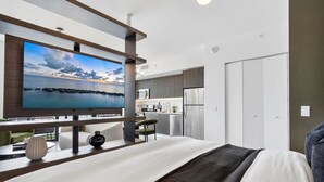 A modern hotel room with a large bed, a TV mounted on a wooden beam, a kitchenette, and a view of the sea. - Downtown Miami Getaway (Miami)