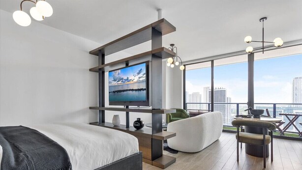 A modern hotel room with a large bed, a flat-screen TV, a seating area with a view of the city, and a balcony with a table and chairs. - Downtown Miami Getaway (Miami)