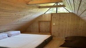 Una piccola camera da letto mansardata con pareti in legno, un letto singolo, una panca e una finestra.