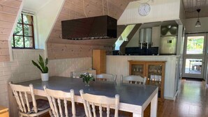 Zona pranzo con tavolo e sedie in legno, una pianta in vaso e una cucina sullo sfondo.