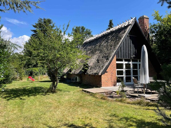 Ett lantligt hus med ett halmtak, en tegelmurad skorsten och ett stort fönster.