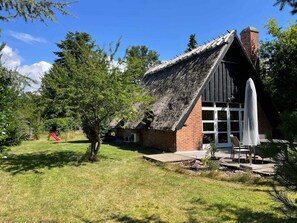 Ett lantligt hus med ett halmtak, en tegelmurad skorsten och en vit dörr.