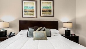 Un lit bien fait, avec du linge de lit blanc, deux tableaux abstraits encadrés au-dessus, et des lampes de chevet de chaque côté.
