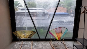 A room with a large window, two chairs, a patterned rug, and a metal stand. - Hotel Lleras Park III (Medellín)