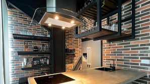A modern kitchen with a brick wall, a central island with a built-in stove, and copper chairs. - Hotel Lleras Park III (Medellín)