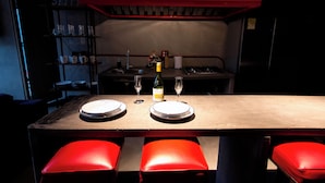 A restaurant with a wooden table set for two, red cushioned chairs, and a red ceiling. - Hotel Lleras Park III (Medellín)