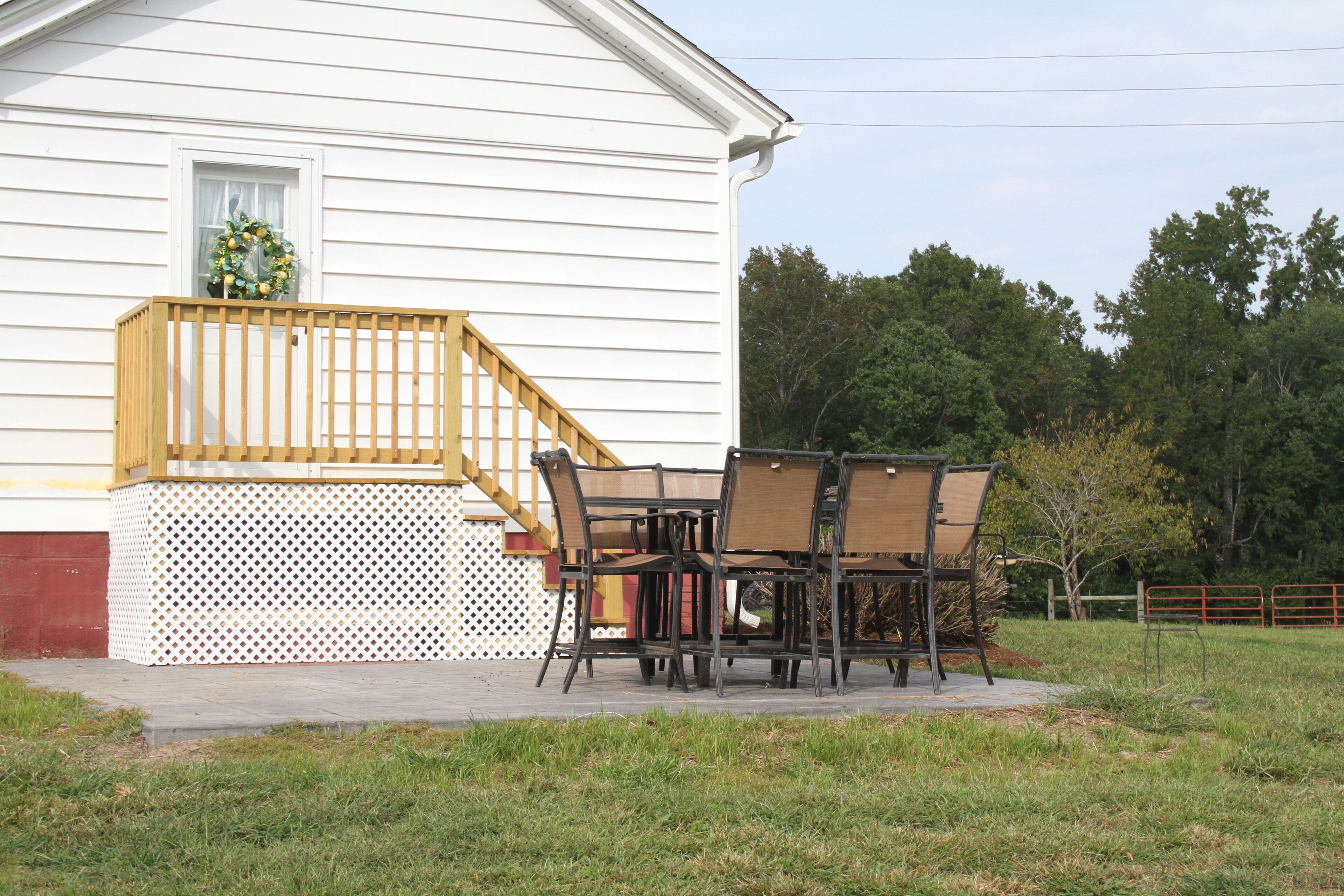 A white house with a wooden deck, a dining table with chairs, and a wreath on the window.