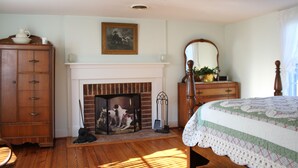 Une chambre avec une cheminée, des meubles en bois, un lit recouvert d’une courtepointe et un miroir.
