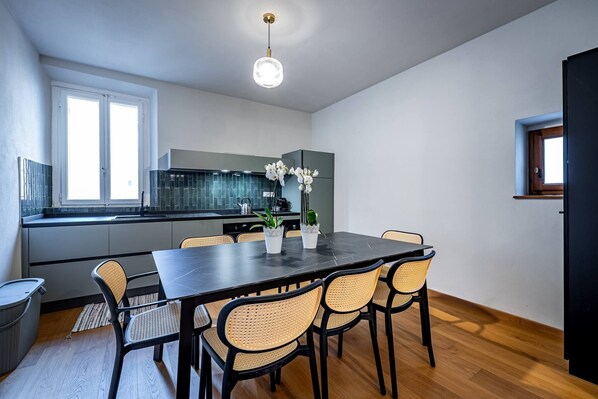 Una cucina moderna con zona pranzo, con tavolo nero, sedie in vimini e piante in vaso.