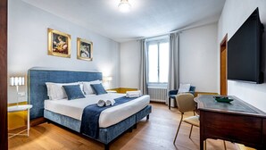 Ein Hotelzimmer mit Bett, Nachttischen, Schreibtisch, Stuhl, Fernseher und einem Fenster mit Vorhängen.