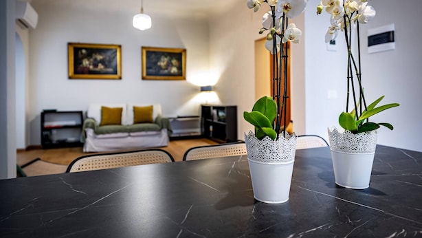 Una sala de estar moderna con una mesa de mármol negro, dos jarrones de orquídeas blancas, un sofá y una lámpara.