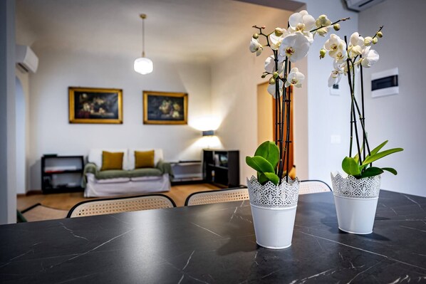 Egy modern nappali, melyben található egy fekete márvány asztal, két fehér orchidea, egy kanapé és egy lámpa.