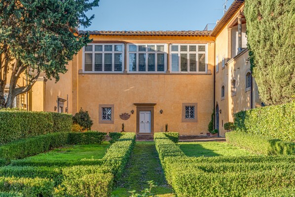 Un edificio con fachada simétrica, entrada central y un jardín bien cuidado con setos.