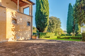 Un patio con suelo empedrado, un edificio con ventanas de arco y árboles altos y delgados.