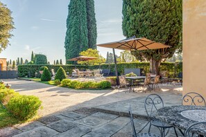 Un patio al aire libre con suelo de piedra, mesas redondas, sillas y sombrillas.