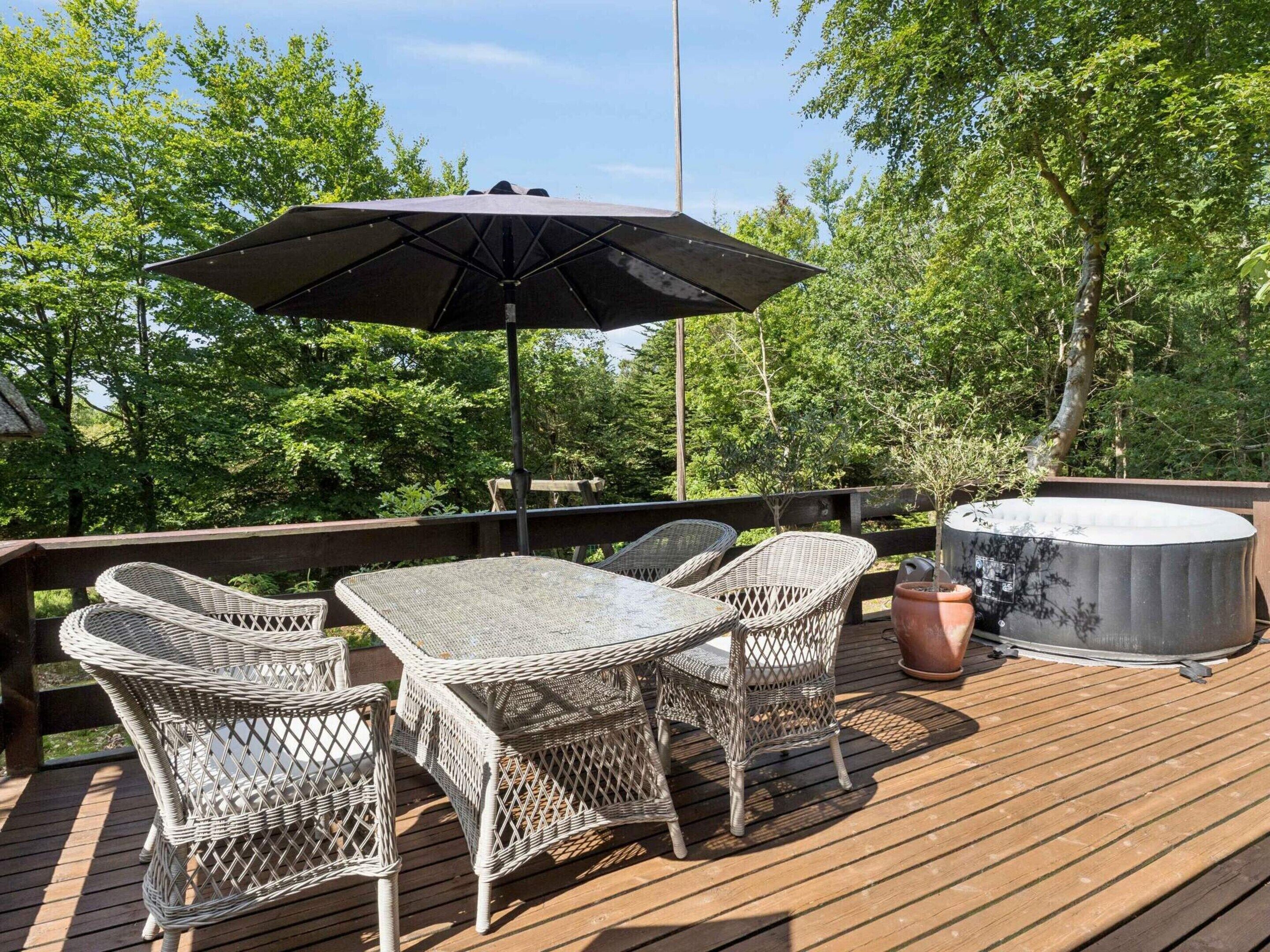 A deck with wicker furniture, a table, chairs, an umbrella, and a hot tub.